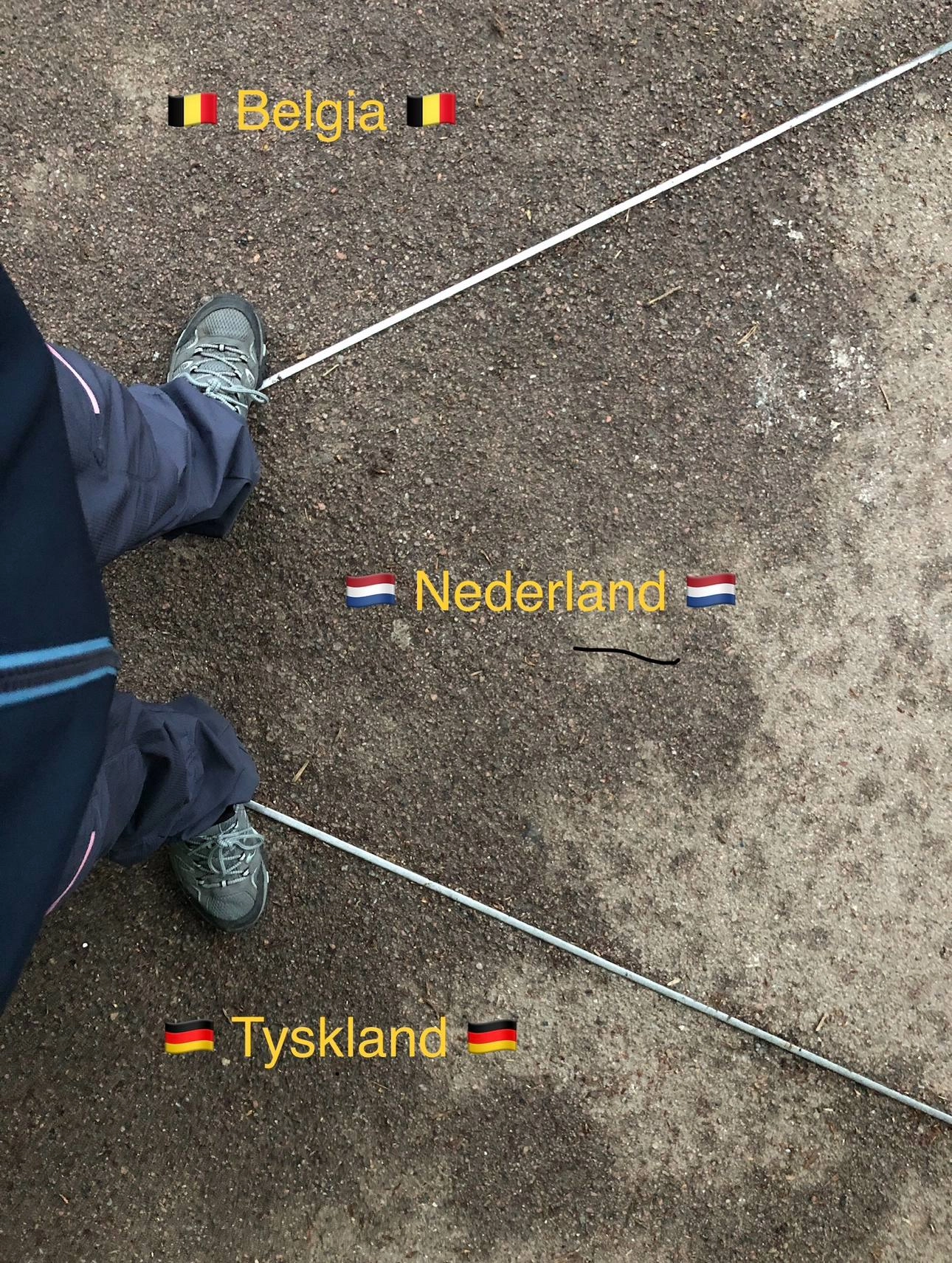 Geocacher standing at the border point where Belgium, the Netherlands, and Germany meet, with feet firmly planted in all three countries.