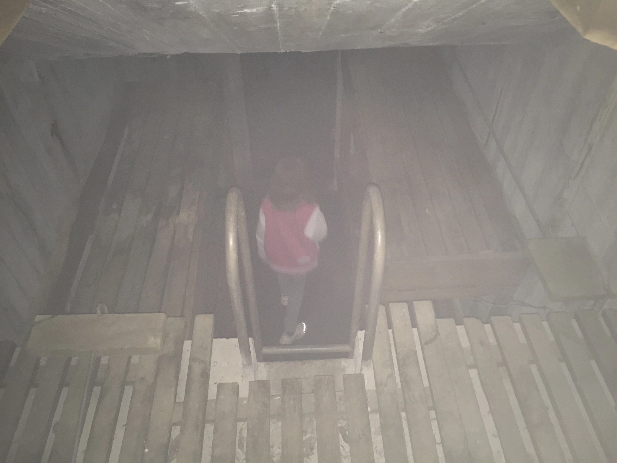 Young girl standing next to narrow metal bunk beds inside a dim, concrete WWII bunker in the Swedish forest.