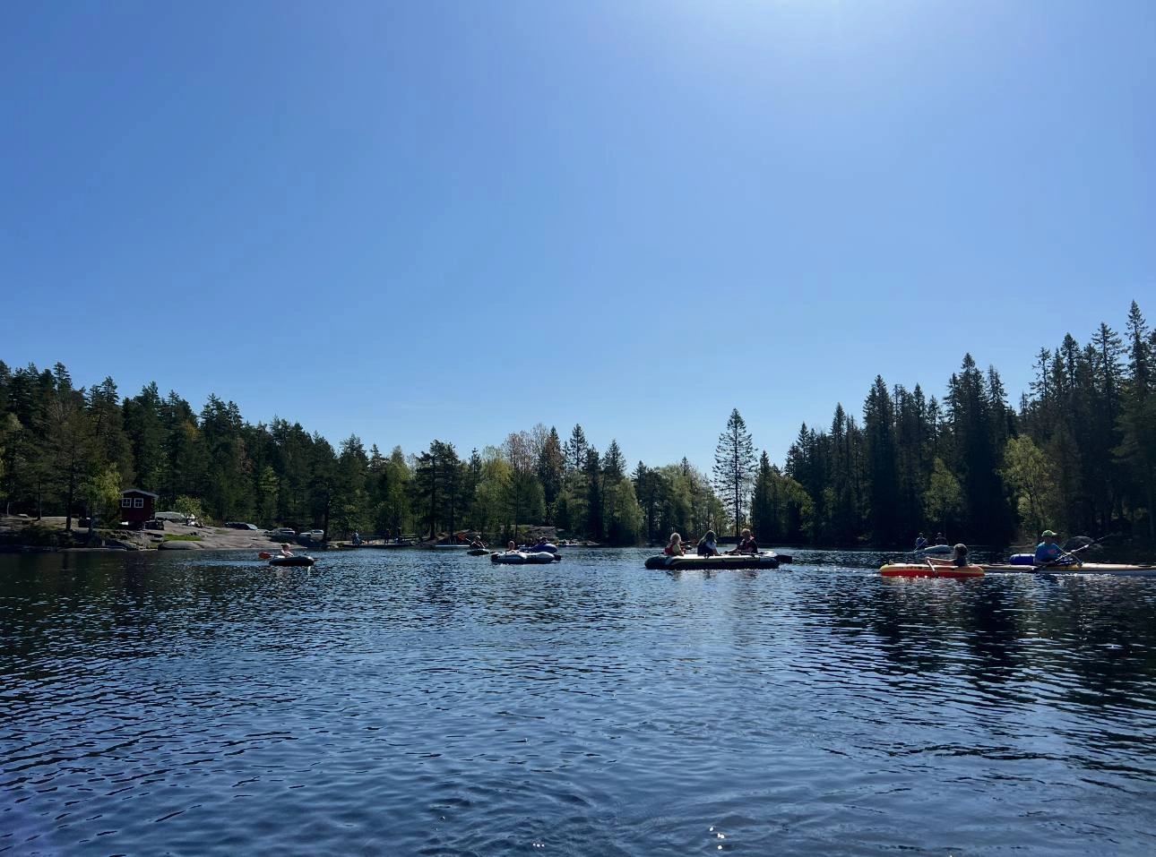 Several geocachers in canoes paddling across a calm lake during a geocaching event, surrounded by nature.