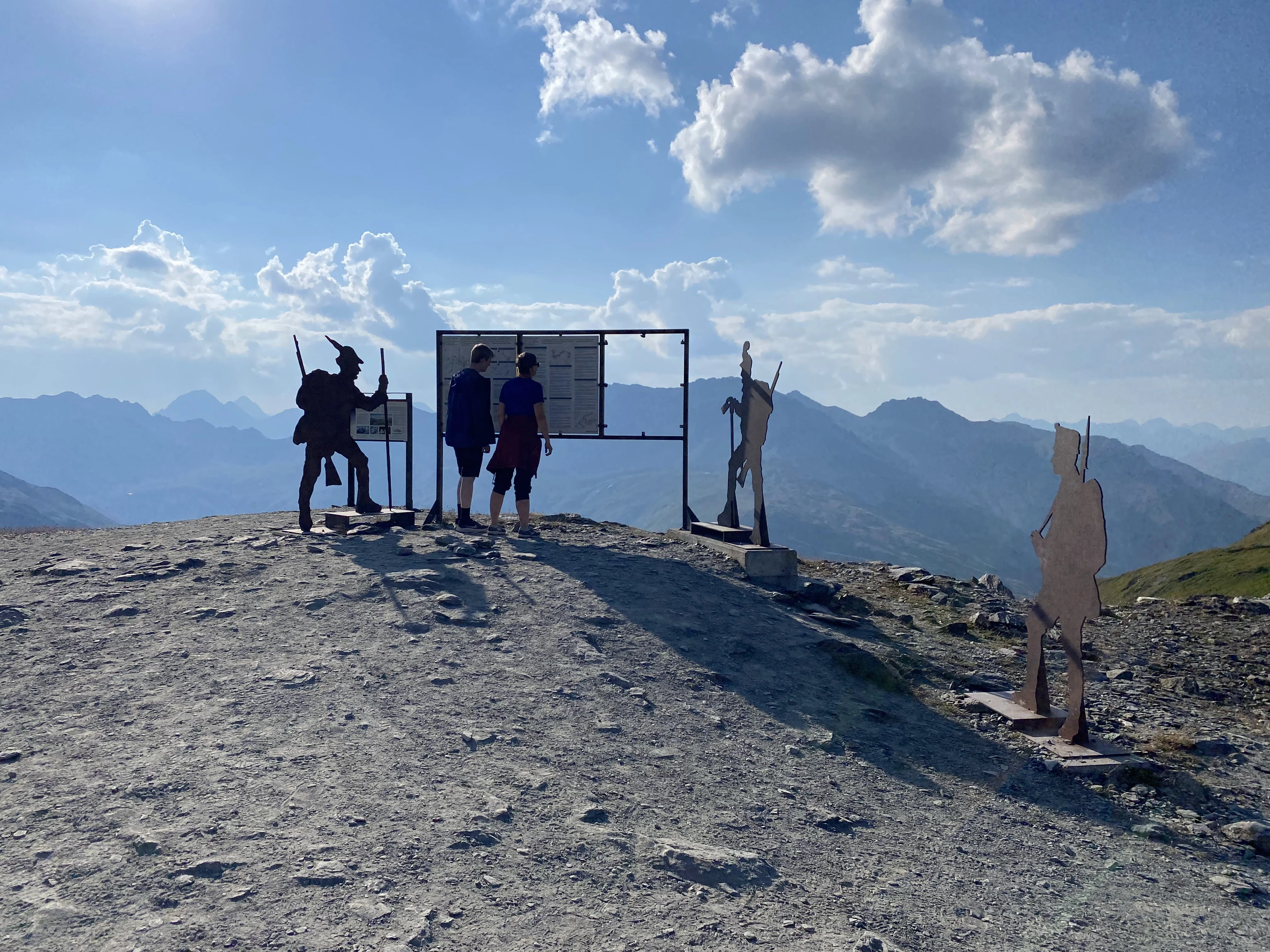 Two geocachers reading an informational sign near the summit of the Stelvio Pass, trying to solve an EarthCache.