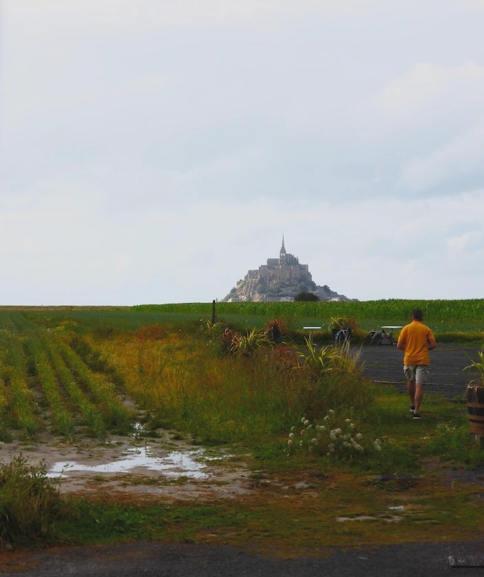 Scenic view of Mont-Saint-Michel rising in the distance as seen from the mainland parking area, across the wide tidal flats.