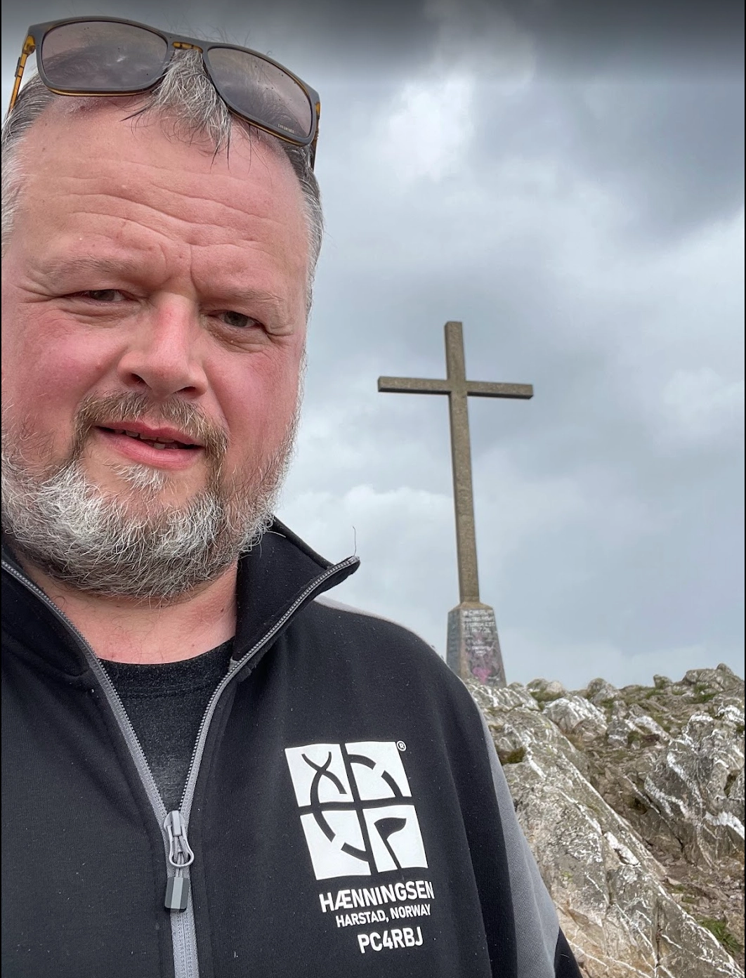 Person standing at the summit of Bray Head next to the iconic cross, with sweeping views of the Irish coastline in the background.